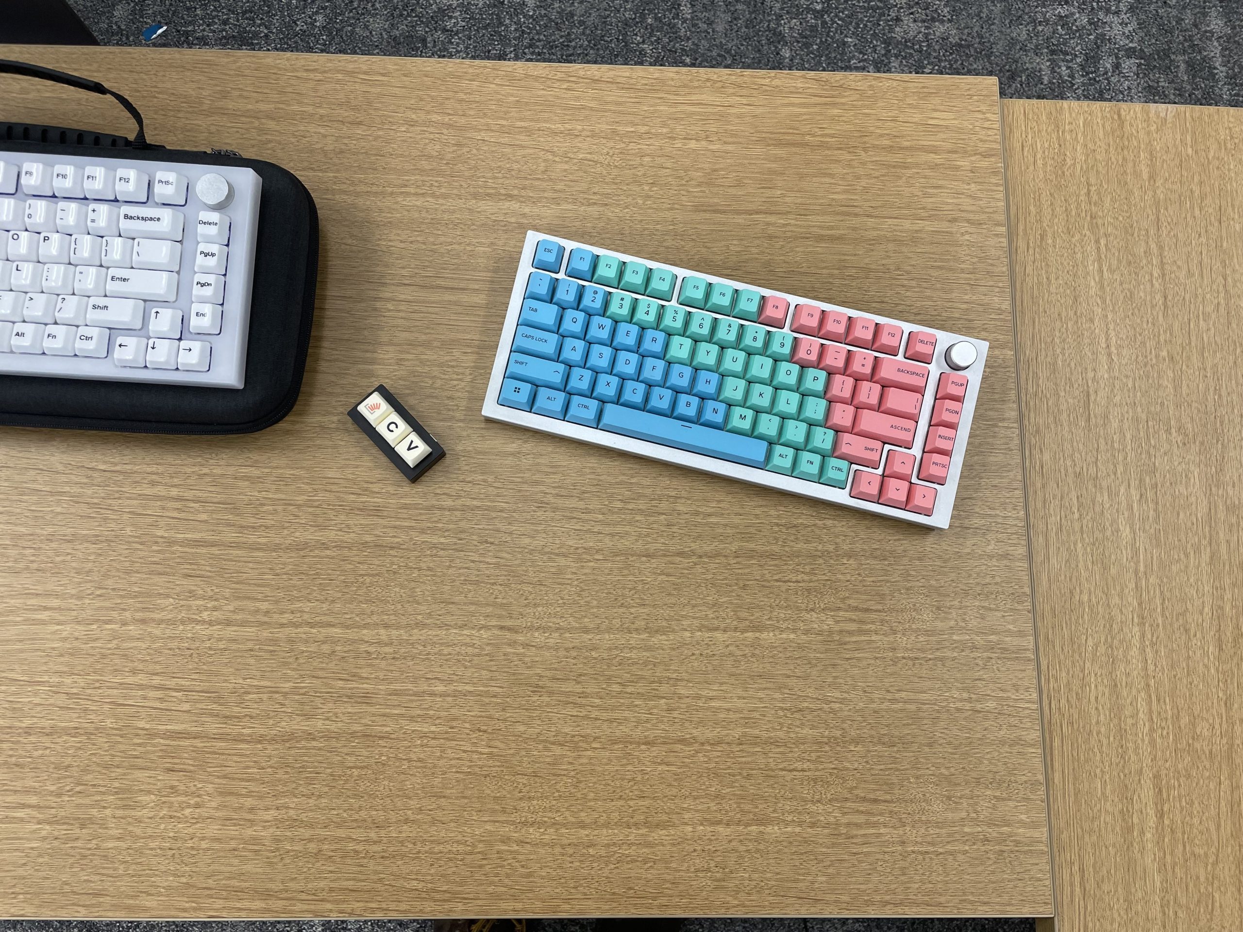 An attendee's keyboards. This user likes knobs. The keycaps on one are blue, green, and red. On the other the keycaps are a uniform black-on-white. Between them is a three-key macropad with the keys Command (or Control), C, and V.